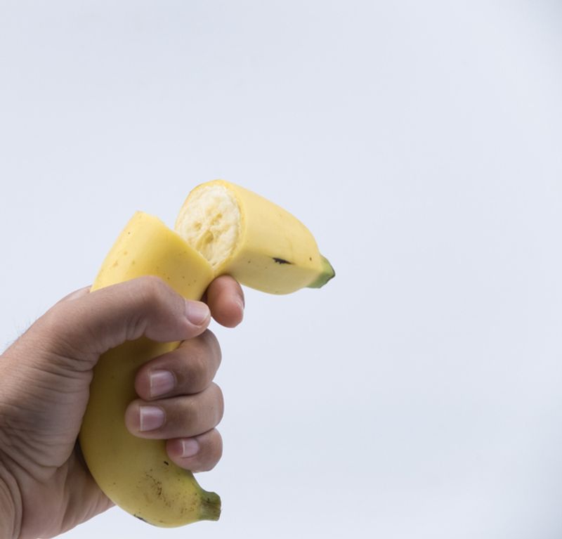 A hand is pictured holding a yellow banana which is broken in half.