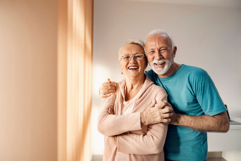 An elderly couple appear with the man hugging the woman over the shoulders.