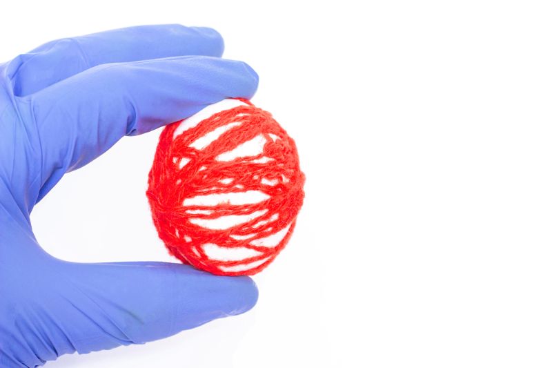 Blue surgical gloved hand holding red yarn in the shape of an egg