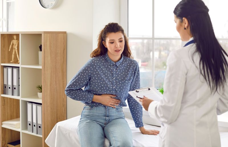 Woman holding hands over stomach speaking with doctor