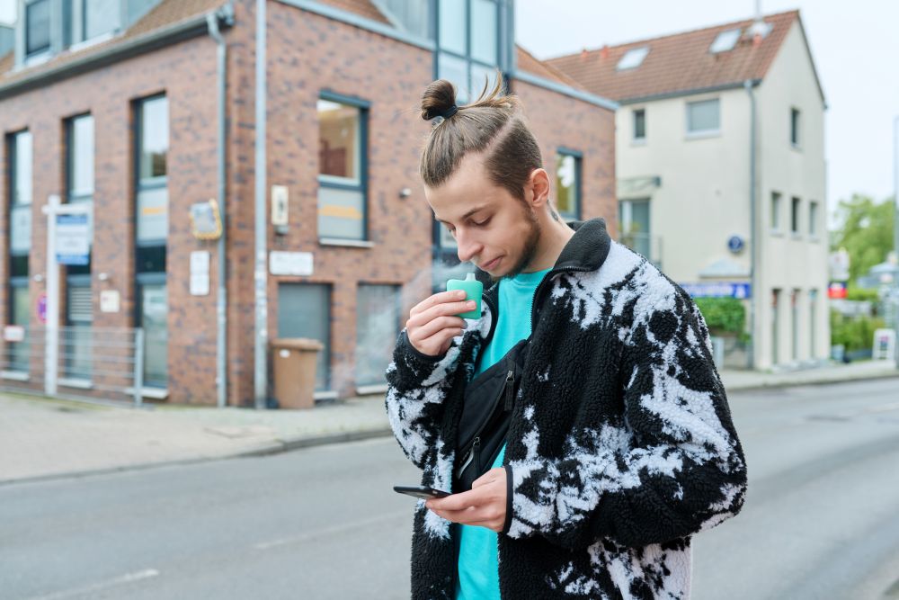 man with high man bun, vaping while on his phone